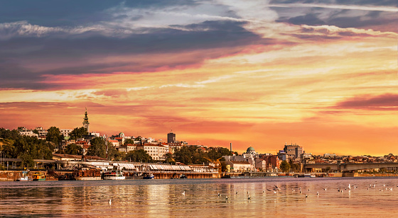 Belgrade Sunset Panorama with Tourist Nautical Port, ancored Nautical Vessels, old Port Depot, Kalemegdan Park, and Downtown skyline with the Church of St. Michael bell tower, viewed from Sava river perspective.