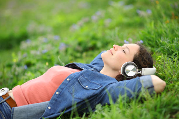 Relaxed woman lying on the grass listening to music stock photo