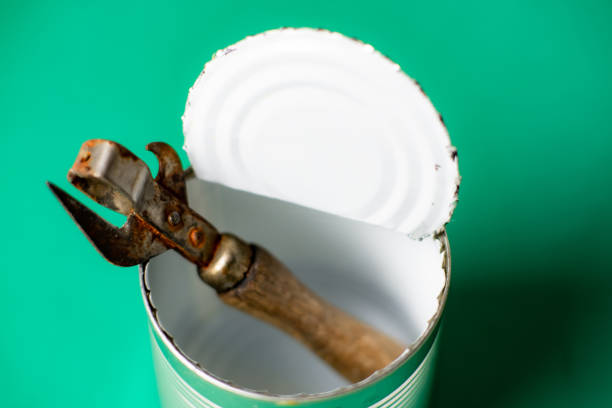 Opened empty tin can and a rusty bottle opener on a green background.