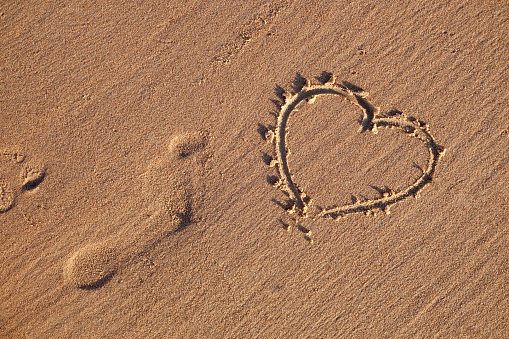Heart symbol drawn on the beach and sand human footprints