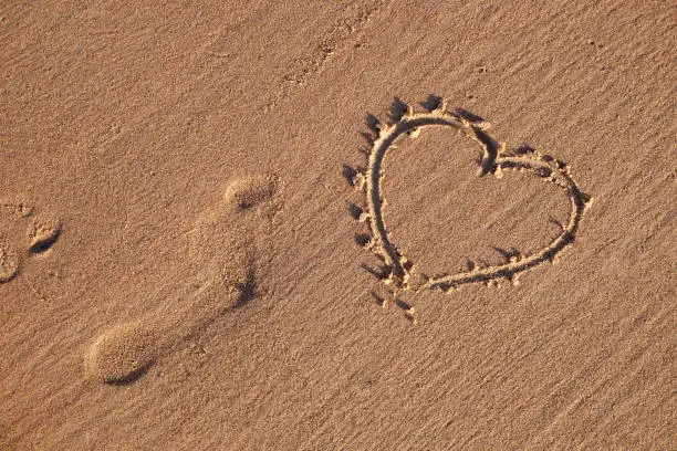 Photo of Heart symbol drawn on the beach and sand human footprints