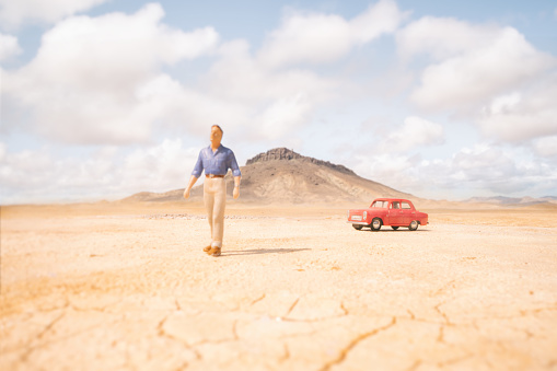 A man walking away from his car in a vast empty desert. Scale model photography.