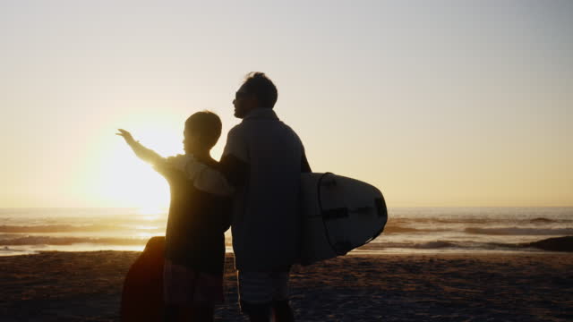 Silhouette father and son with surfboard on sunny sunset beach
