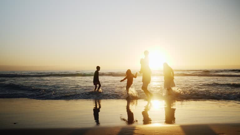 Silhouette family playing in ocean surf on sunset beach