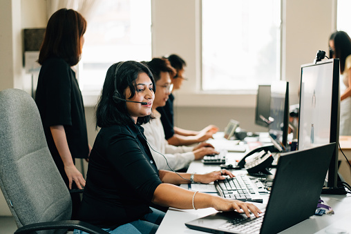 business person from multiracial group wearing headset and using computer while sitting with colleagues