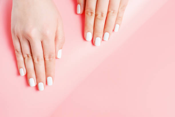 istock Female hands with white manicure on pink background, top view 1394209500
