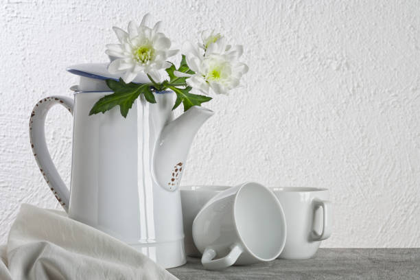 White ceramic teapot with two white and black cups on a wooden table on a gray wall