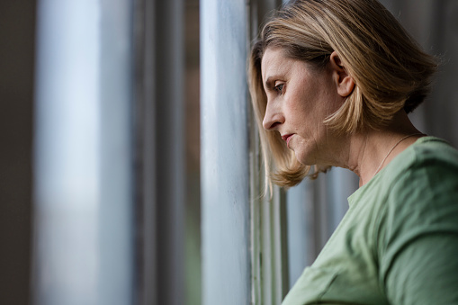 A close up side view of a woman having a quiet moment of solitude and contemplation as she looks out of a window with a sad look on her face.