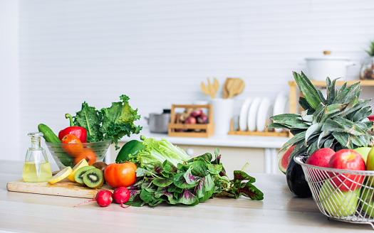 Background of green vegetables, fruits, lemon, kiwi, cherries and red tomatoes for good health decorated on wooden table in cozy white clean kitchen with copy space. Healthy food and interior Concept