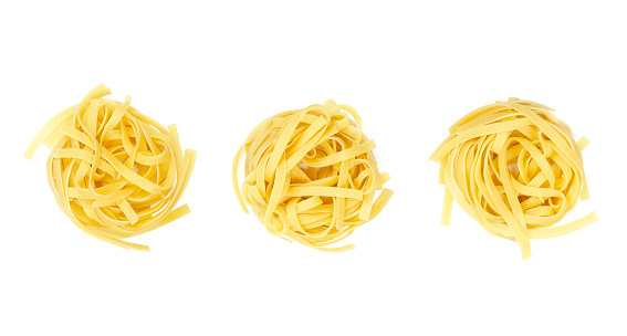 Three uncooked tagliatelle pasta nests, in a row, from above, on white background. Dried, raw traditional Italian type of egg pasta. Long, flat ribbons, about 6 mm wide, twisted into a small nests.