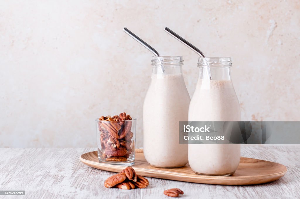 Pecan milk in glass bottles with reusable metal drinking straw Alternative non dairy homemade pecan milk in glass bottles with reusable metal drinking straws. Pecan nut milk on wooden tray Pecan Stock Photo