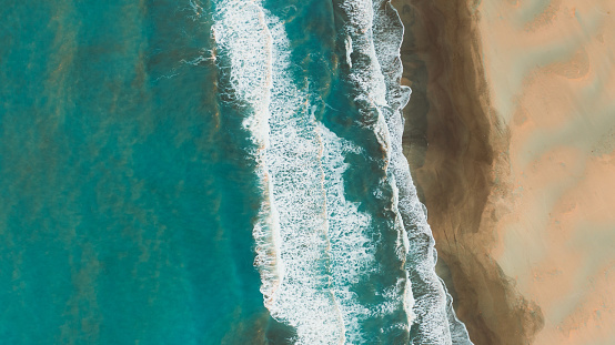 Drone photo of the textured-like crystal blue sea with waves and the sand dunes meeting the sea in Patara, South Turkey