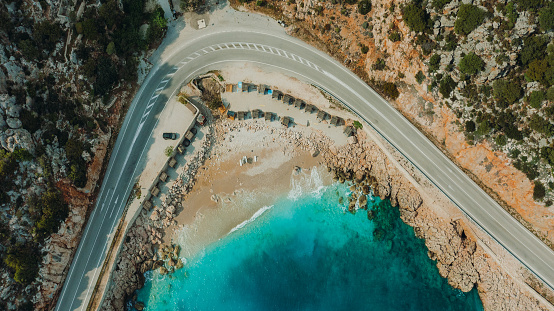 Scenic drone photo of the highway pas surrounded by the mountains, white sand beach and the crystal blue sea with parked car in Antalya region, South Turkey