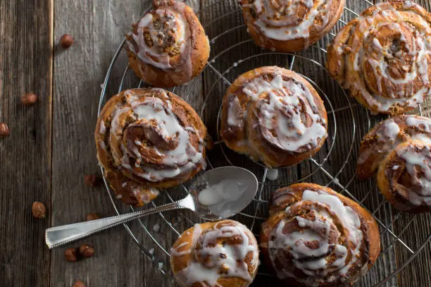 Fresh and homemade baked cinnamon rolls with sugar icing and hazelnuts. Served on a cooling rack isolated on wooden table background.