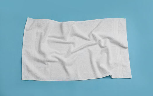 Crumpled white beach towel on light blue background, top view