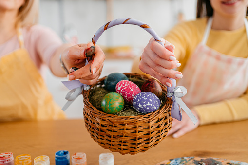 Mother and a young daughter sitting at home and holding a basket with Easter Eggs for Easter. Close-up.