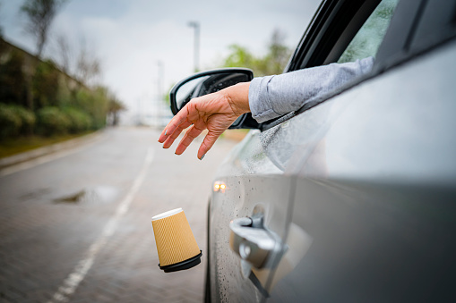 Rear view of a driver hand throwing a disposable coffee cup out from car window in a road. High resolution 42Mp outdoors digital capture taken with SONY A7rII and Zeiss Batis 40mm F2.0 CF lens