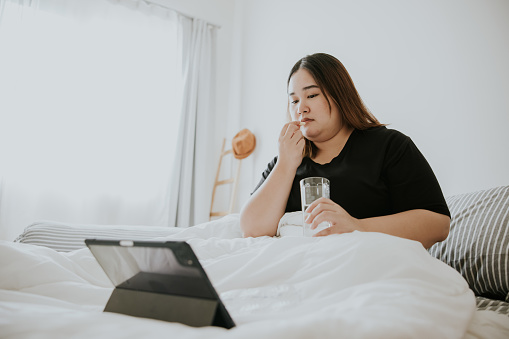 Telemedicine service, Young adult woman eating flu medicine before taking a nap.