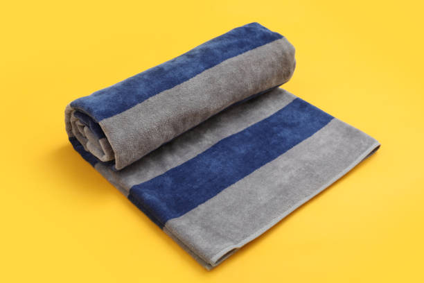 Rolled striped beach towel on yellow background