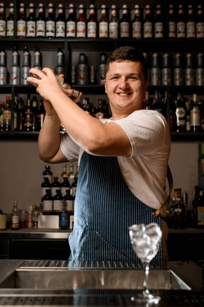 istock Bartender professionally holds by two hands glassy shaker with cold alcoholic cocktail and shakes it. 1394231139