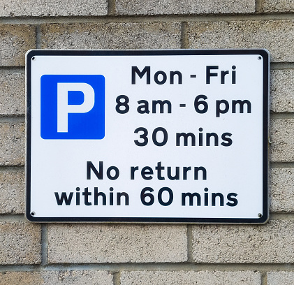 A sign in a British town detailing weekday street parking restrictions.