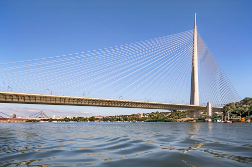 aerial motion past pylons and lacy cables of cable-stayed bridge cars speed above water against city line and clear sky