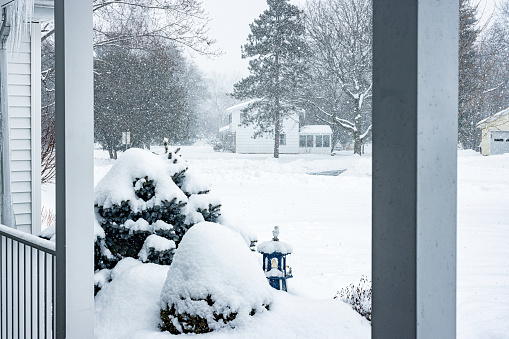 View outside beyond a suburban residential home's porch columns at the neighborhood during a February blizzard snow storm in western New York State.