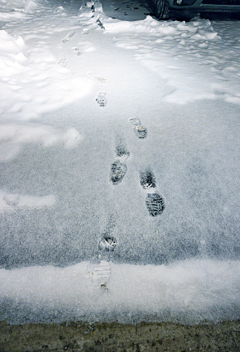 Dark footstep footprints in light winter snow on a residential home driveway after returning home.