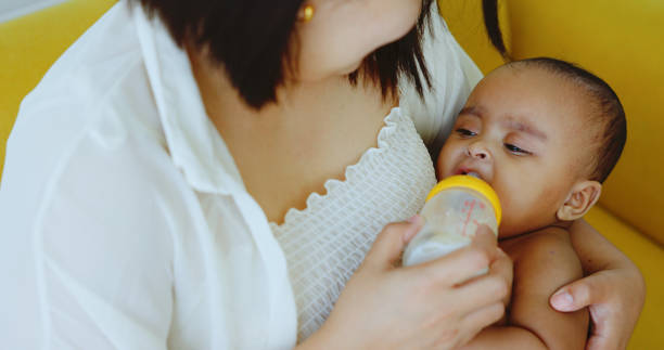 criança afro-americana está amamentando leite fome nos braços da mãe em casa. cuide da comida para recém-nascido. cuidar de crianças durante seus anos de crescimento com nutrição de qualidade. amor mãe para a filha - 25 30 years adult african descent bonding - fotografias e filmes do acervo