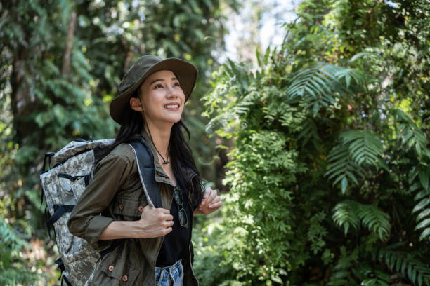野生の森の中を一人で旅するアジアの若い美しい女性バックパッカー。魅力的な女の子の旅行者は、休日の休暇旅行中に幸せと楽しさで自然の木の中を歩きながら、周りを見て探索します。 - fun walk ストックフォトと画像