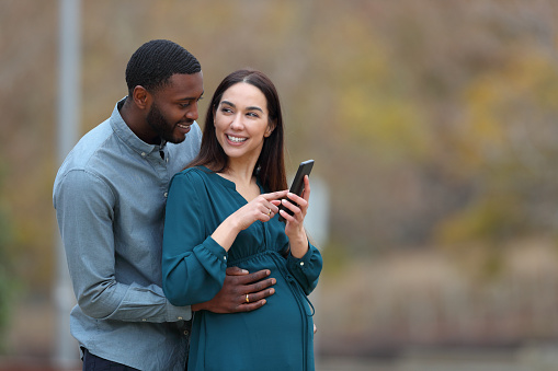 Interracial couple enjoying pregnancy holding phone