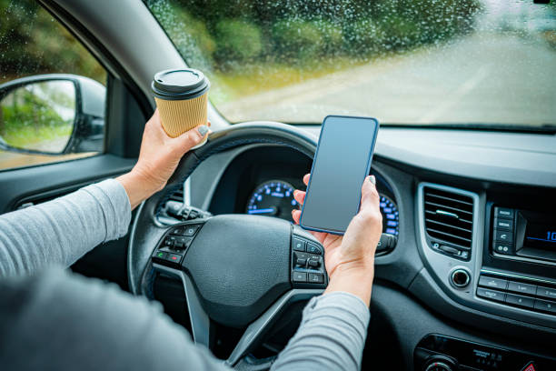 Woman holding disposable coffee cup and mobile phone while driving though wet road in a rainy day. High resolution 42Mp outdoors digital capture taken with SONY A7rII and Zeiss Batis 40mm F2.0 CF lens