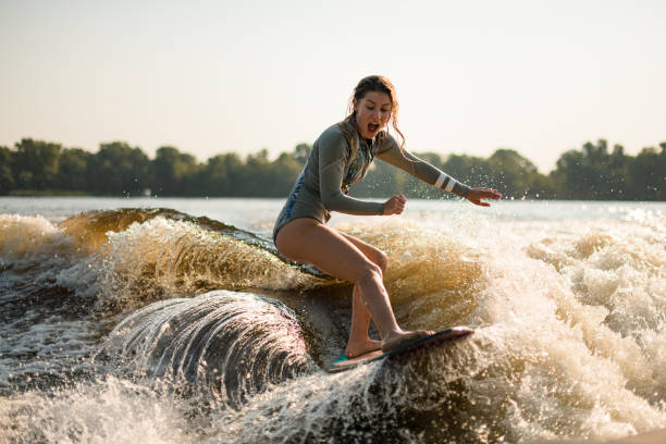 überraschte nasse wakesurferin, die an einem warmen tag auf einer plätschernden welle reitet - wakeboarding stock-fotos und bilder