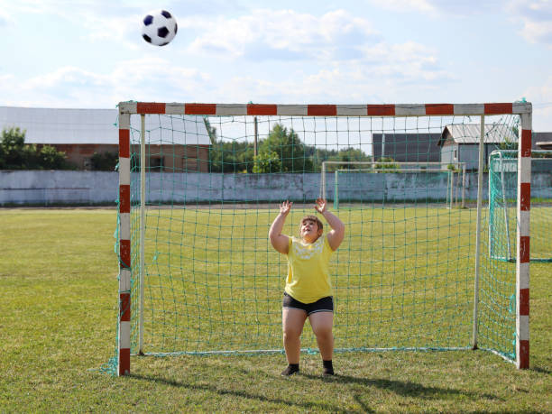 girl with overweight stands in football gate and wants to catch ball with his hands - child obesity imagens e fotografias de stock