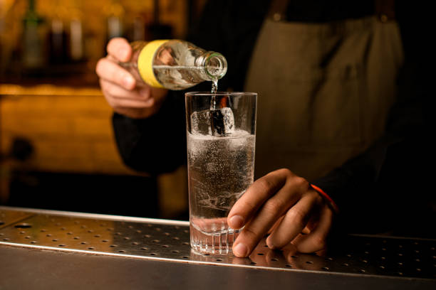 zbliżenie szkła z zimnym napojem i kostkami lodu, do których barman dokładnie wlewa napój z butelki - drinking water drink men zdjęcia i obrazy z banku zdjęć