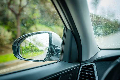 Close up view of external rear-view mirror shot from car interior in a rainy day. Water drops on mirror and windshield. Selective focus on mirror. High resolution 42Mp outdoors digital capture taken with SONY A7rII and Zeiss Batis 40mm F2.0 CF lens