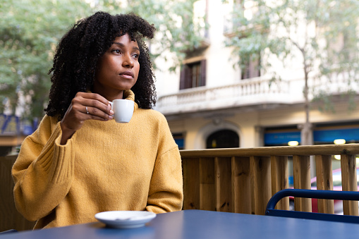 Young African American woman holding coffee cup in outdoors cafe terrace. Copy space. Lifestyle concept.