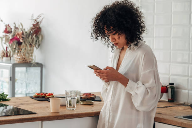 istock Young mixed race woman using mobile phone to send text message at home kitchen. Copy space. 1394257815