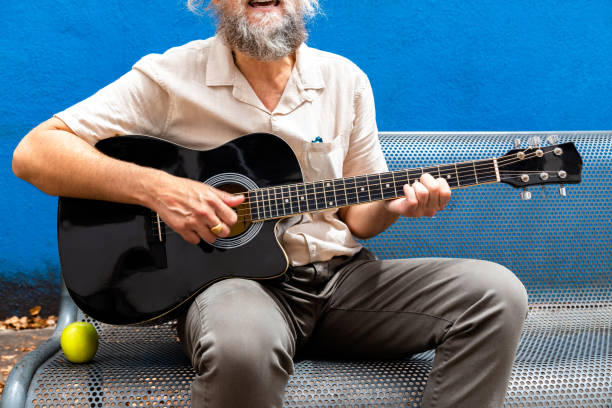 istock Unrecognisable mature man with beard playing the guitar and singing sitting on a bench on blue background. 1394257845