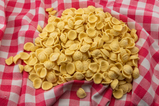 orecchiette pasta auf rot karierter tischdecke - orecchiette stock-fotos und bilder