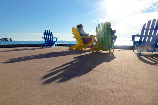Rear view of two women sitting on Adirondack Chairs and watching seascape