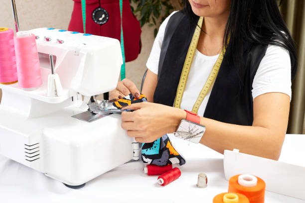 istock Close up of seamstress hand using sewing machine in workshop. Workplace of tailor - sewing machine, rolls of of thread, fabric. 1394265204