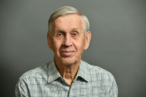 Cute cheerful old man in a shirt, on a gray background.