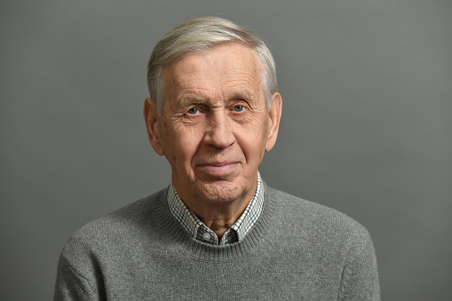Cute cheerful old man in a shirt, on a gray background.