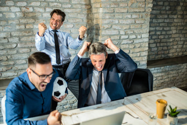 Cheerful businessmen cheering while watching their sports team on computer in the office. stock photo