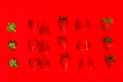 A number of strawberries, whole and sliced against a red background.