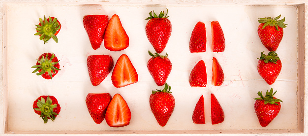A number of strawberries, whole and sliced, on a wooden tray.
