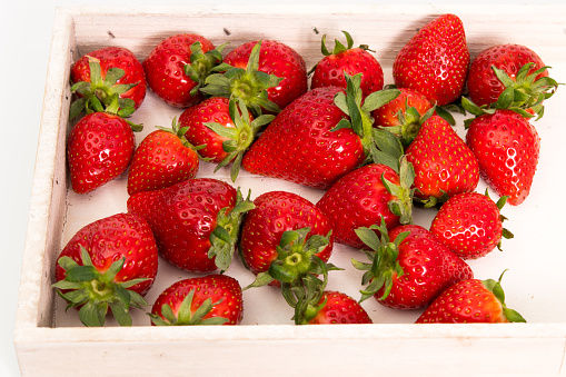 A number of strawberries in a wooden tray on a white background.
