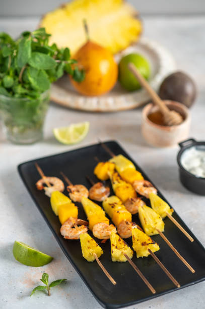 istock Grilled shrimp skewers with pineapple and mango. Shrimp skewers with mint, pineapple, mango, lime and yogurt sauce on a black plate. 1394281941