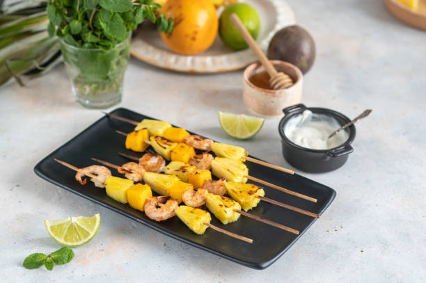 istock Grilled shrimp skewers with pineapple and mango. Shrimp skewers with mint, pineapple, mango, lime and yogurt sauce on a black plate. 1394281943